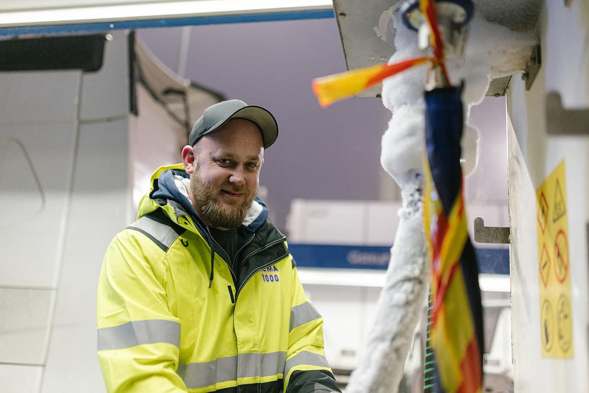 Mann i REMA 1000-jakke smiler ved en frossen kjøleenhet.