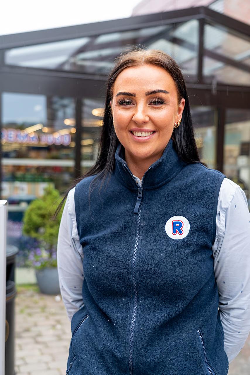 REMA-ansatt smiler iført sin uniform 