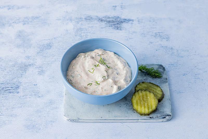 Burgerdressing i liten skål med dill og sylteagurk ved siden av.