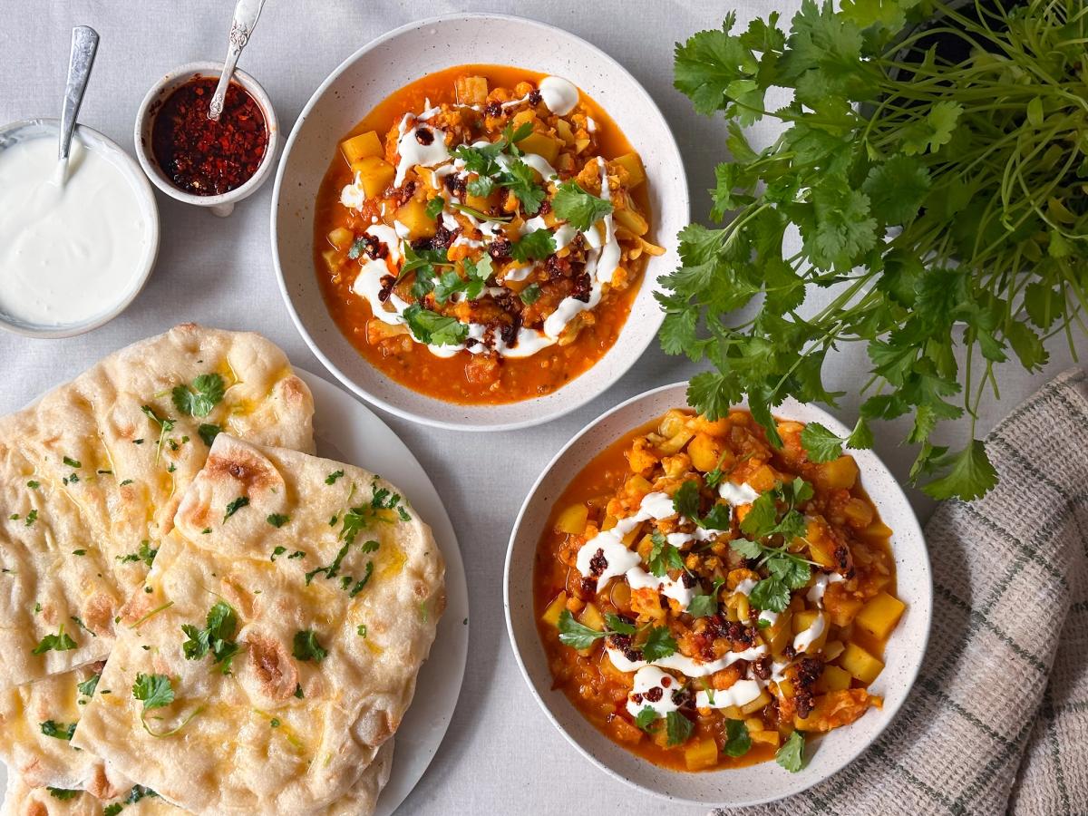 To skåler med krydret grønnsaksgryte, yoghurt og koriander, servert med naanbrød.