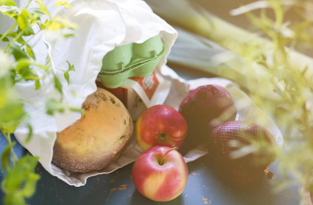 Fire butikkmedarbeidere står foran frukt- og grøntavdelingen i en dagligvarebutikk. Hyller med ferske grønnsaker vises i bakgrunnen, og et blått skilt med teksten «GRØNNSAKER» henger over avdelingen.