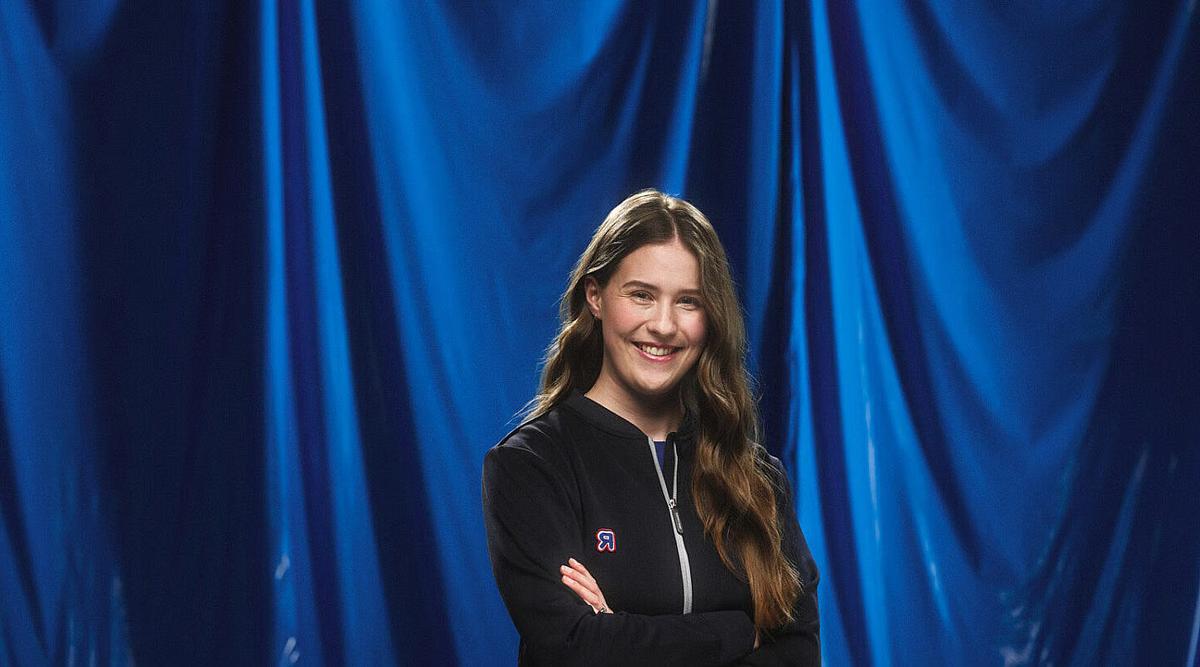 Smilende kvinne i REMA-jakke foran blå bakgrunn