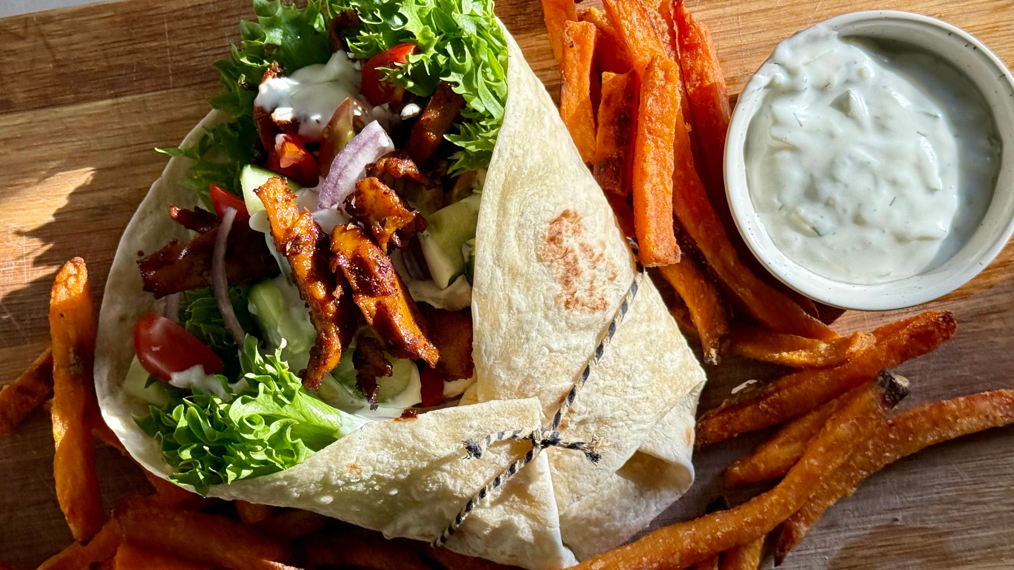 Bilde av gyros med grønnsaker og søtpotetfries på en trefjøl