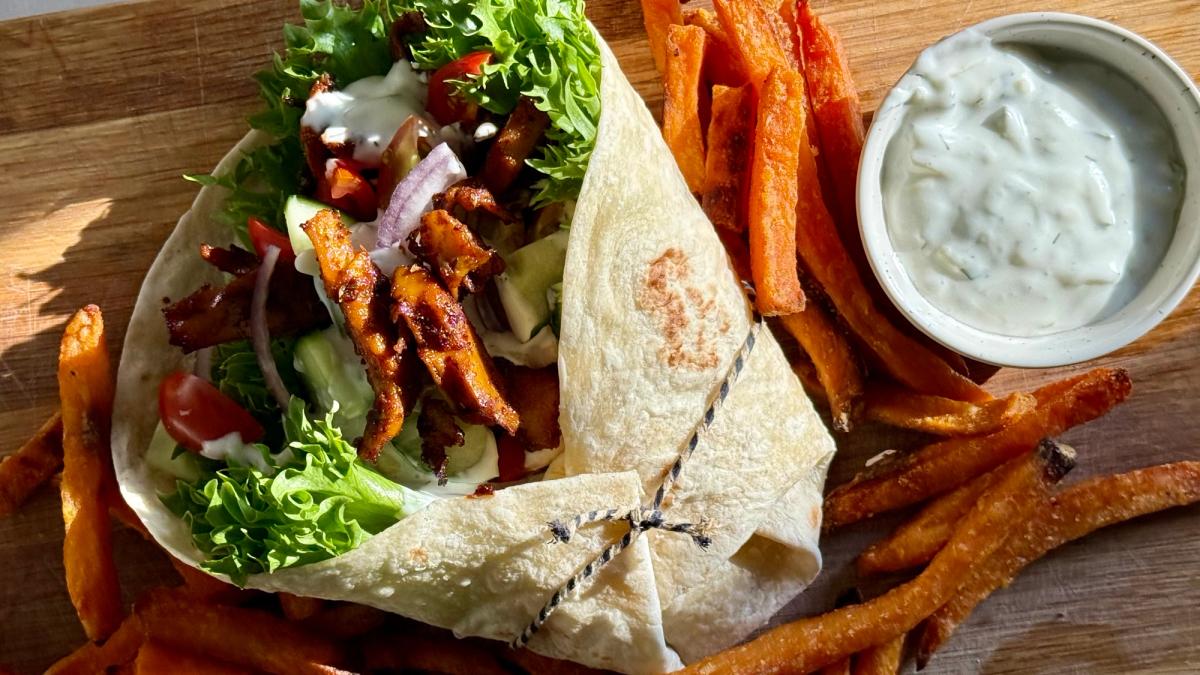 Bilde av gyros med grønnsaker og søtpotetfries på en trefjøl