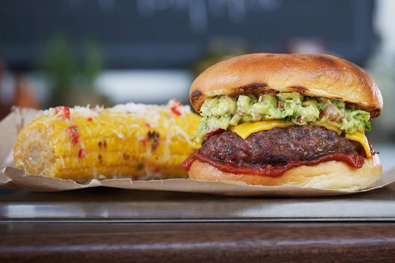 Hamburger med ost, guacamole og ketchup, servert med maiskoble. 