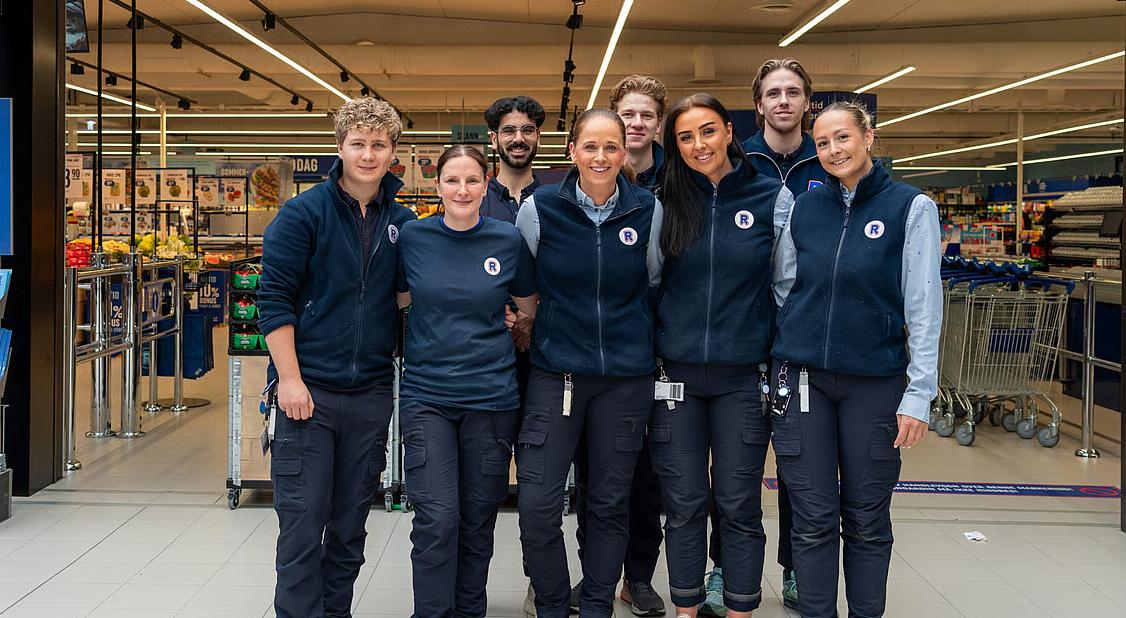 Bilde av REMA 1000 ansatte som står foran butikk og smiler