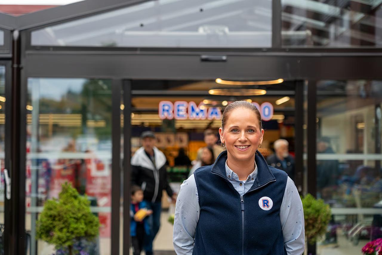 REMA 1000 ansatt utenfor butikk som smiler