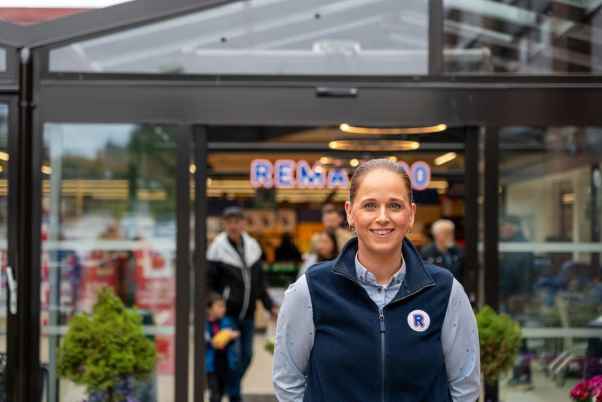 REMA 1000 ansatt utenfor butikk som smiler