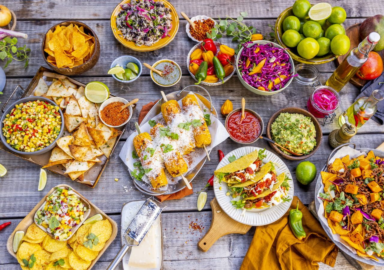 Dekket bord sett ovenfra med tacolefser, kjøttdeig, guacamole, salsa, rømme, revet ost og friske grønnsaker i små skåler
