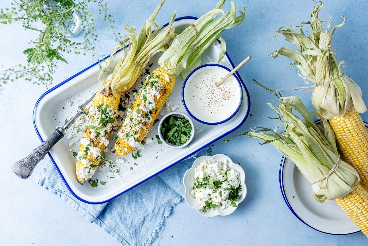 Elote er meksikanske maiskolber. Disse er servert på rektangulært serveringsfat med dressing ved siden av.